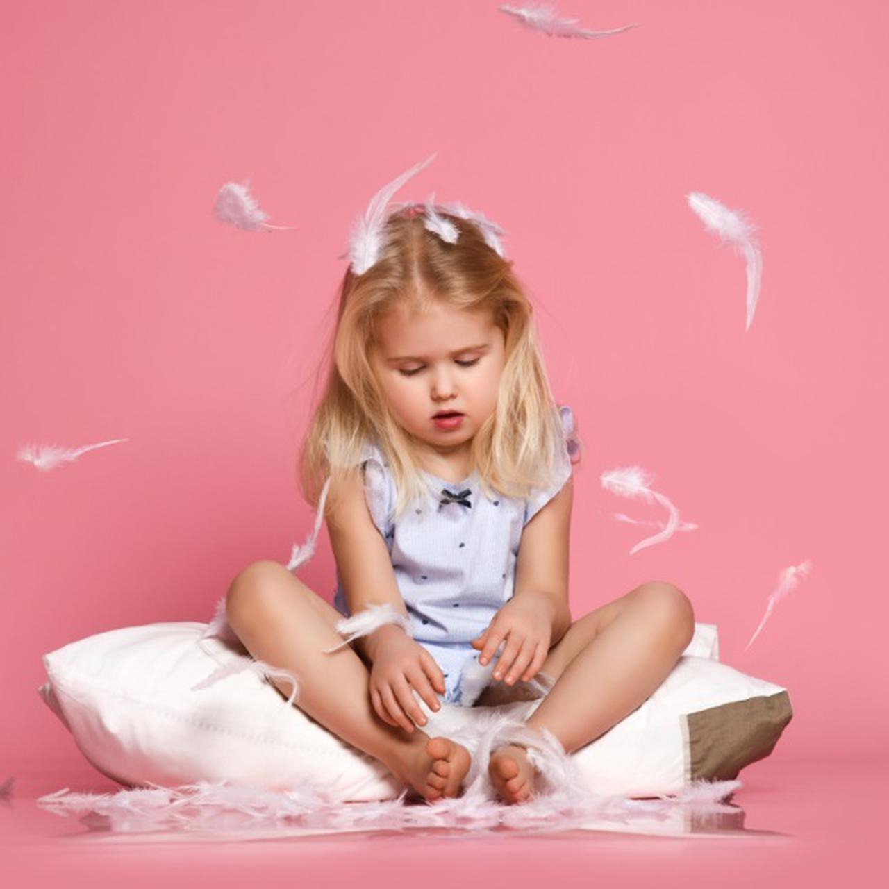 Funny-small-child-Light-hair-sitting-White-Pillow-feeling-Joy-catching-Feathers-having-fun-cute-Blue-eyed-girl